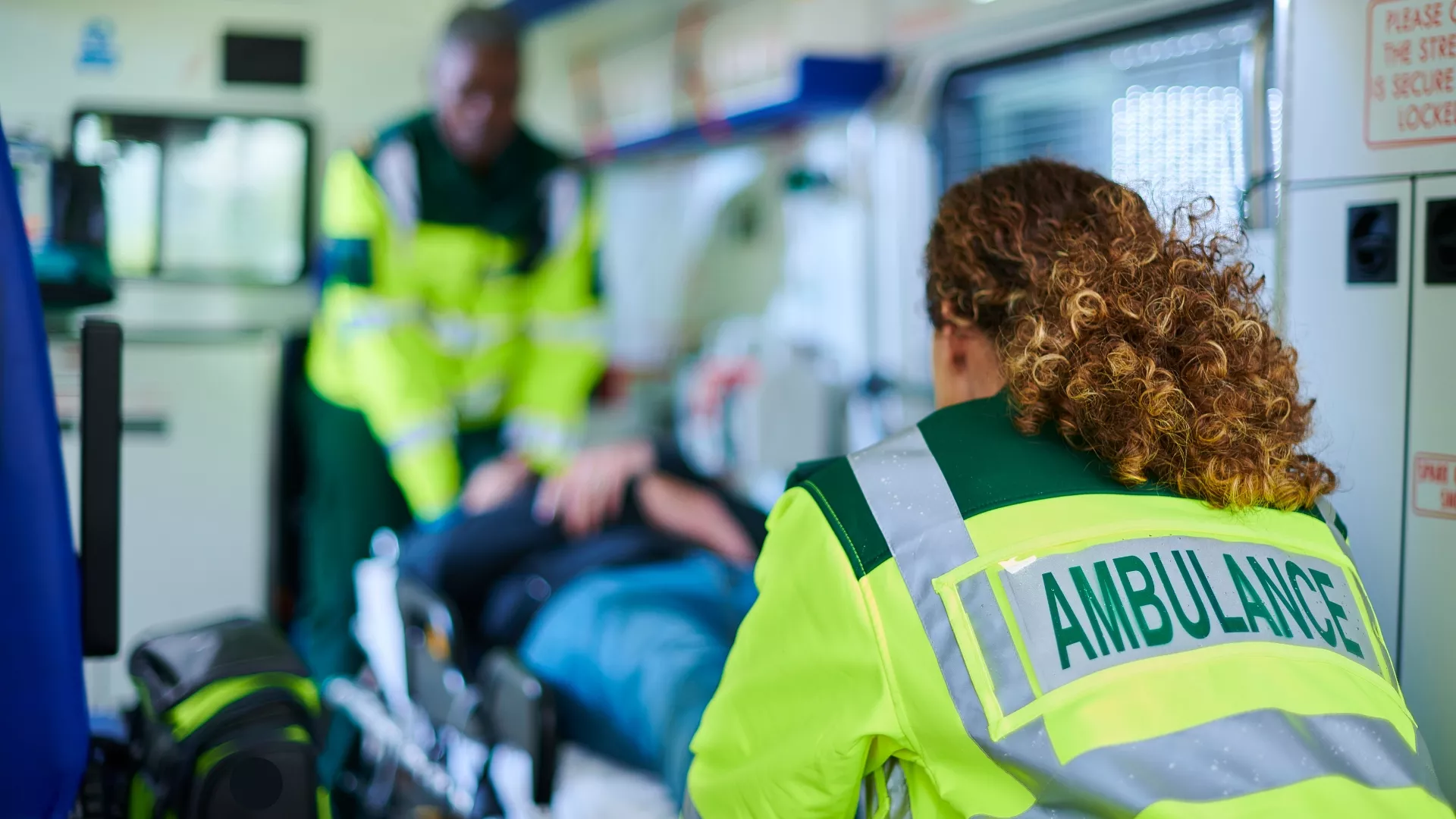 Ambulancière de dos qui pousse un patient sur un brancard pour entrer dans une ambulance