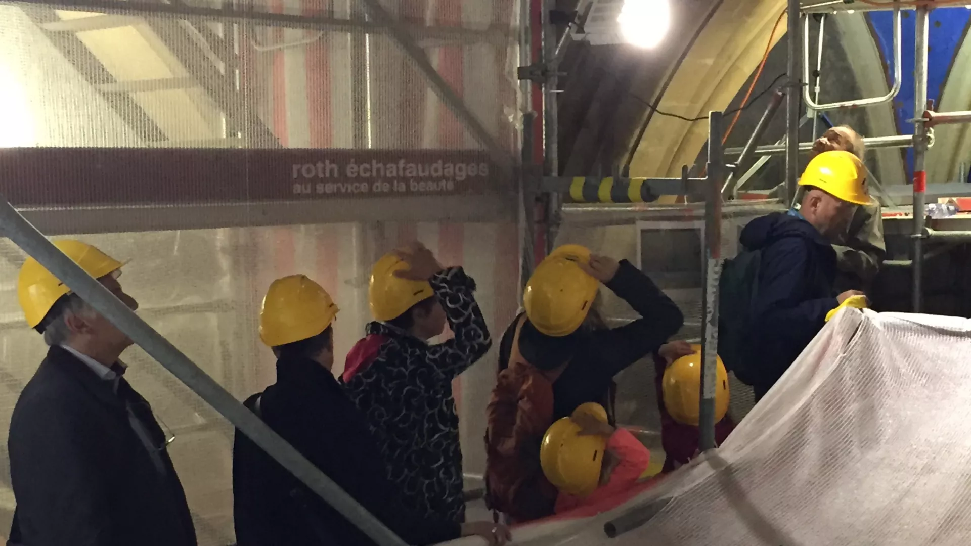 Personnes coiffées de casques jaunes visitant les échafaudages de la Collégiale