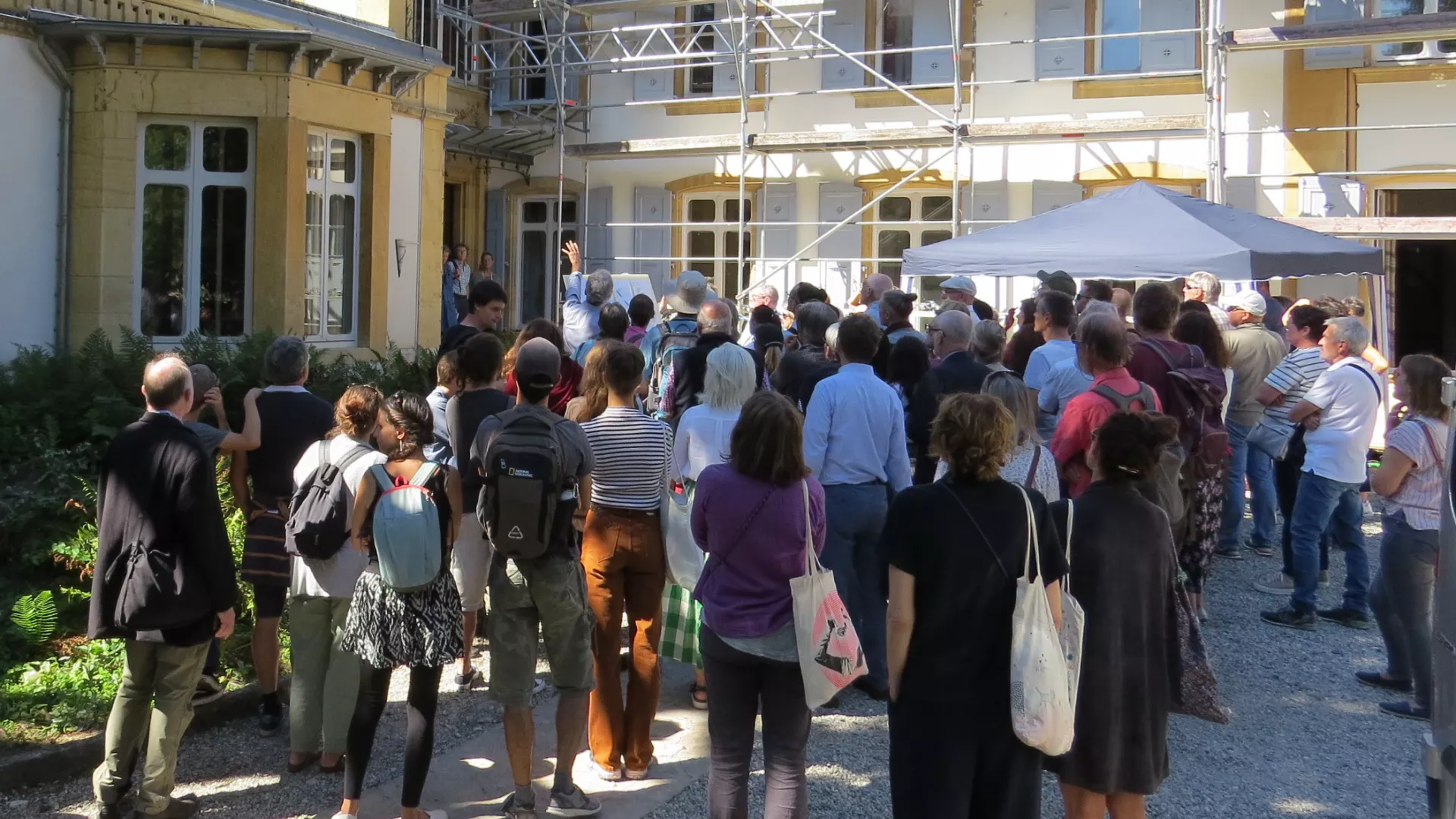 Public écoutant les explications devant un bâtiment anciens