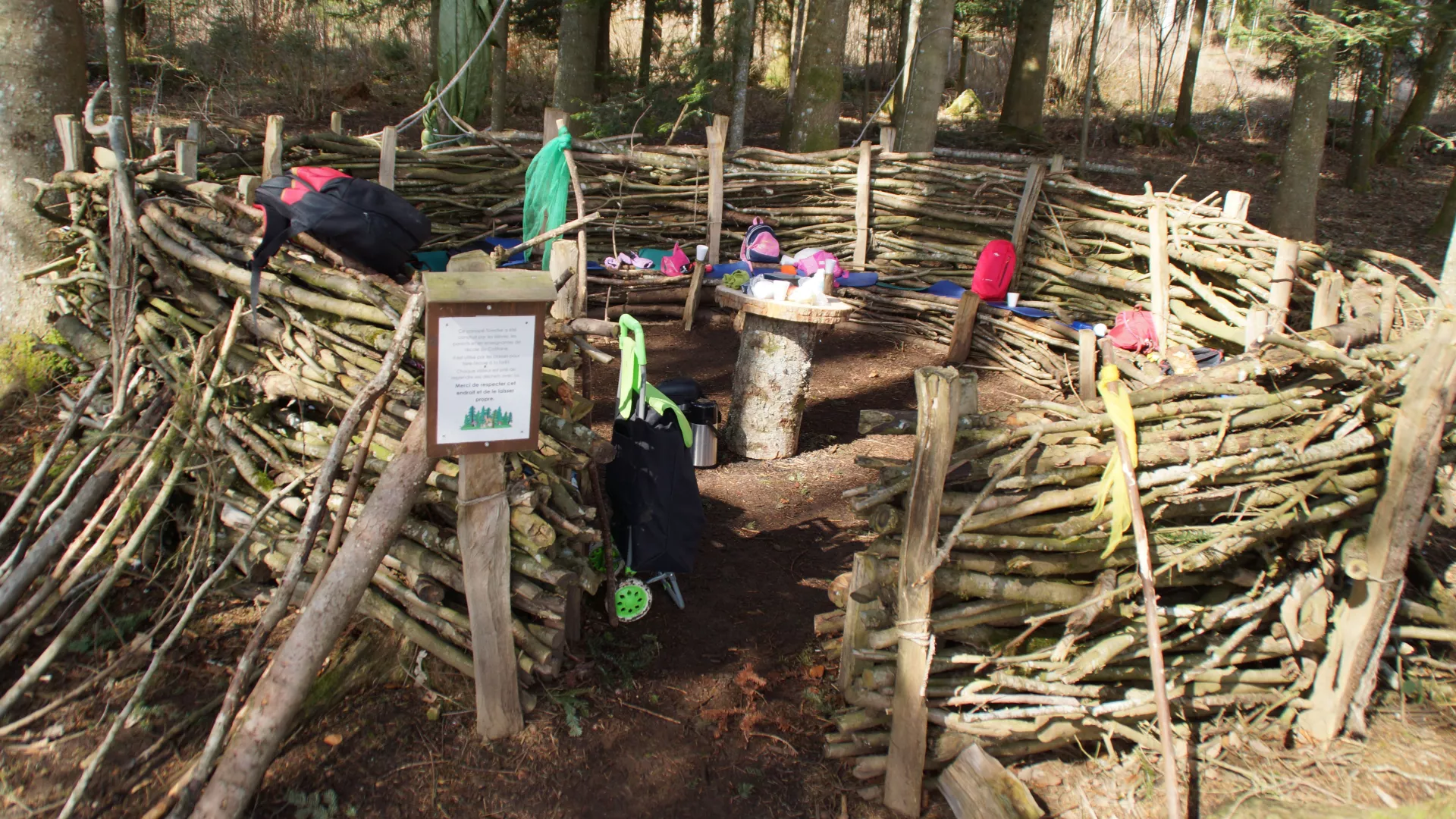 Canapé forestier fait d'un cercle de branchages empilés entre des piquets. Des rondins servent de petites tables.